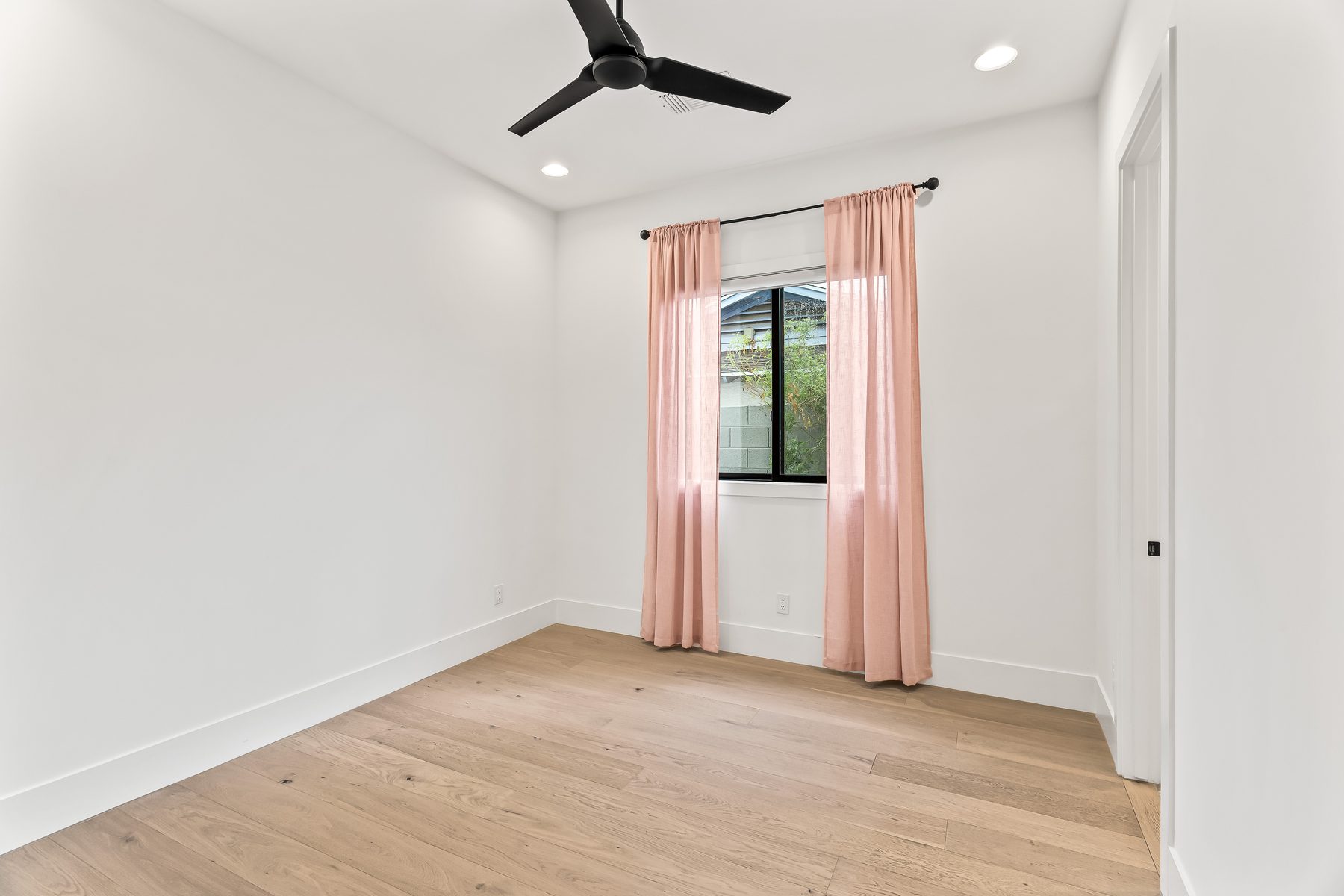 Bedroom with oak floors, ceiling fan, and black-framed window in Arcadia, Phoenix